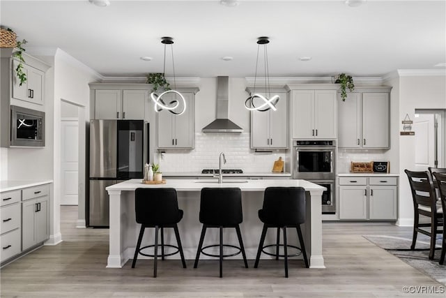 kitchen with decorative light fixtures, a kitchen island with sink, gray cabinetry, and wall chimney range hood