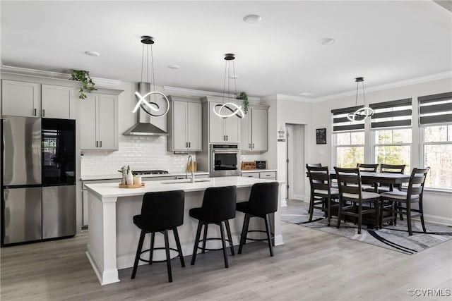 kitchen featuring wall chimney exhaust hood, a breakfast bar, stainless steel appliances, sink, and gray cabinets