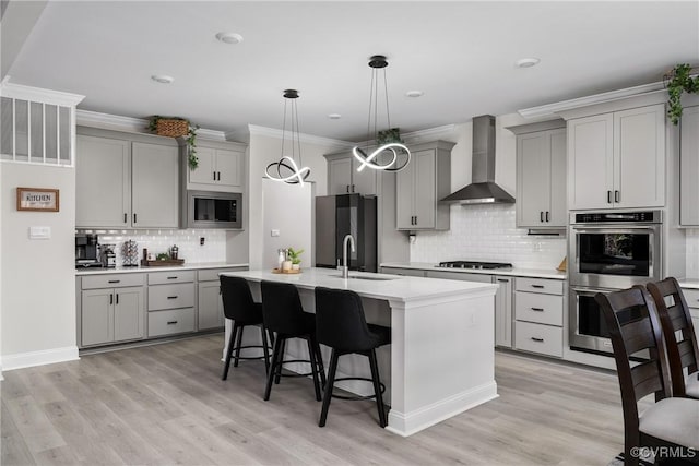 kitchen featuring gray cabinetry, light wood-type flooring, wall chimney range hood, and stainless steel appliances