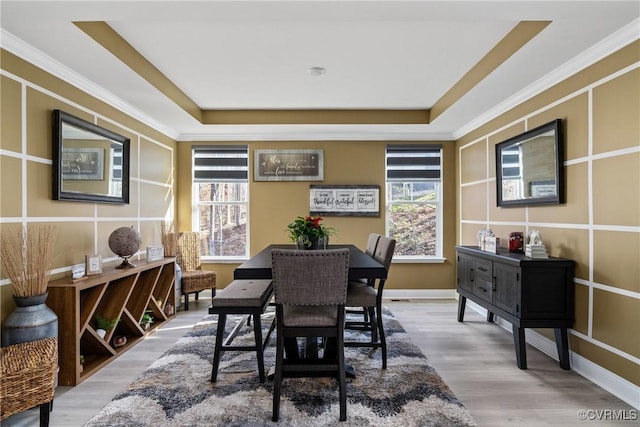 dining space with light hardwood / wood-style floors, ornamental molding, and a tray ceiling