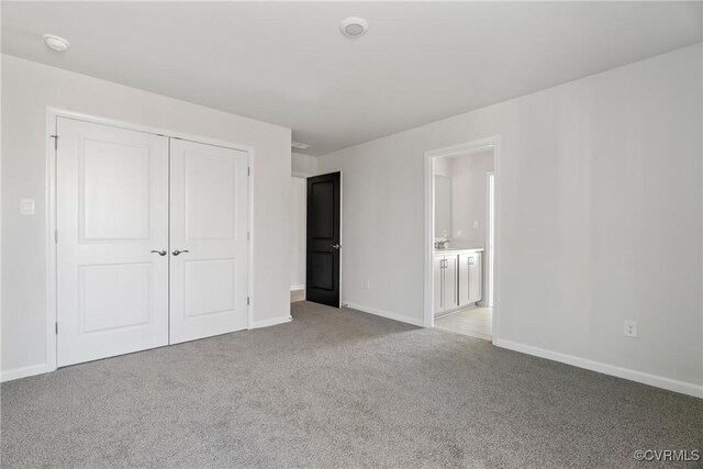 unfurnished bedroom featuring ensuite bath, a closet, and light colored carpet