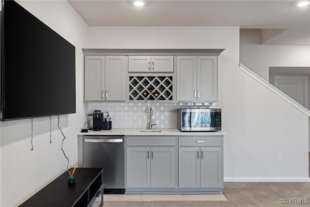 bar featuring gray cabinets, decorative backsplash, sink, and appliances with stainless steel finishes