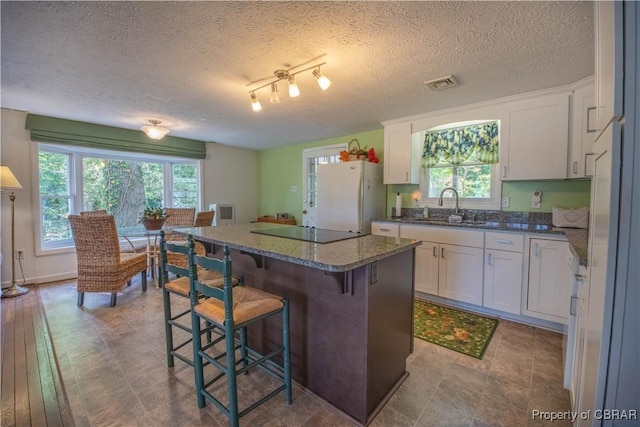 kitchen with a center island, sink, white fridge, black electric cooktop, and white cabinets