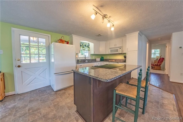 kitchen with white cabinetry, a kitchen breakfast bar, dark stone countertops, white appliances, and a kitchen island