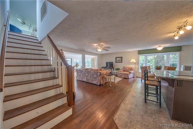 living room with ceiling fan, wood-type flooring, a textured ceiling, and a wood stove