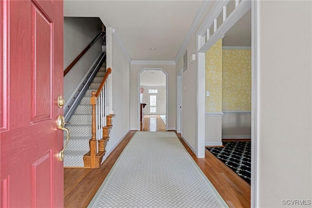 entryway featuring arched walkways, wood finished floors, baseboards, stairs, and ornamental molding