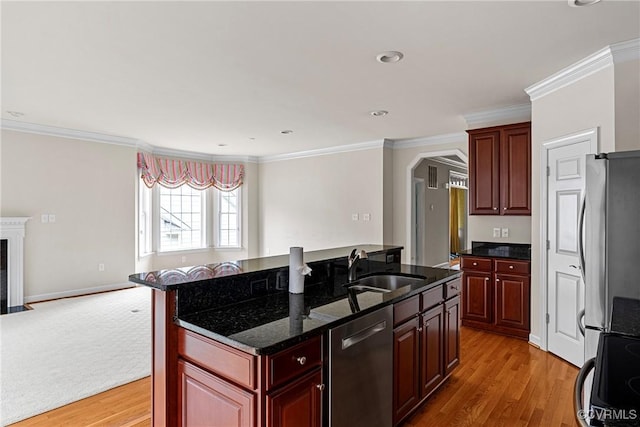 kitchen featuring reddish brown cabinets, a fireplace with flush hearth, a kitchen island with sink, stainless steel appliances, and light wood-type flooring