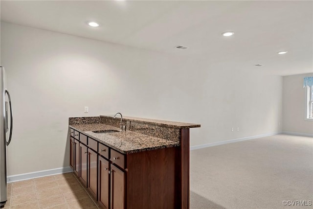 kitchen featuring stainless steel fridge, dark stone countertops, kitchen peninsula, and sink