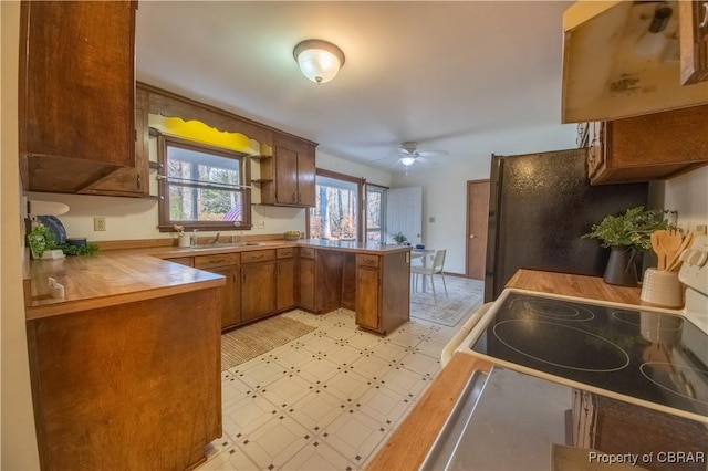 kitchen with kitchen peninsula, wooden counters, ceiling fan, sink, and range