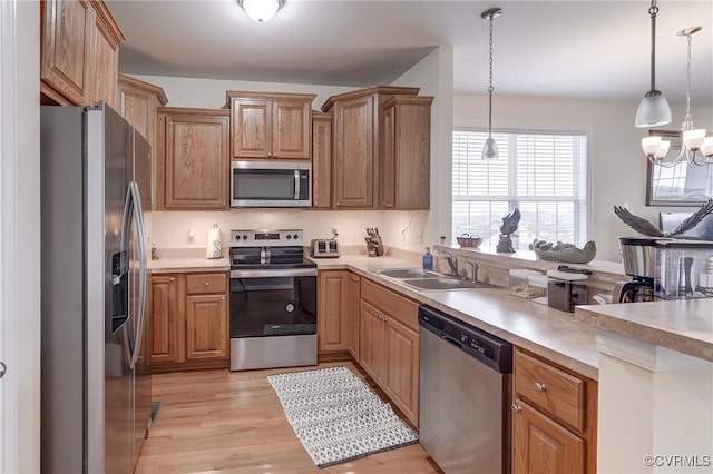 kitchen featuring appliances with stainless steel finishes, light wood-type flooring, sink, an inviting chandelier, and hanging light fixtures