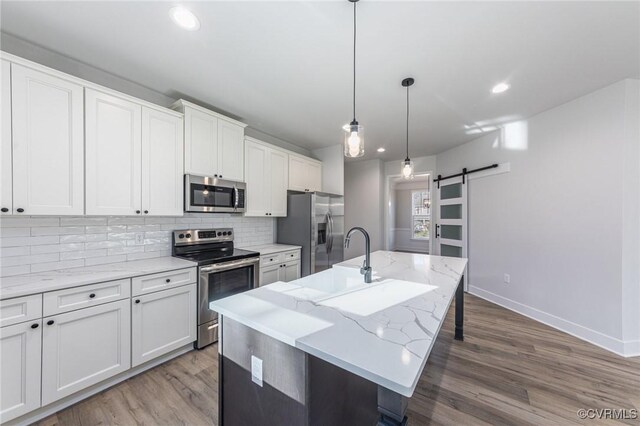 kitchen with a barn door, white cabinets, an island with sink, and appliances with stainless steel finishes