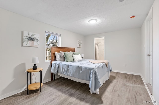 bedroom with a textured ceiling, connected bathroom, and light hardwood / wood-style flooring