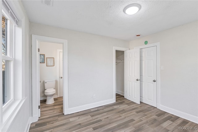 unfurnished bedroom with ensuite bath, a closet, hardwood / wood-style floors, and a textured ceiling