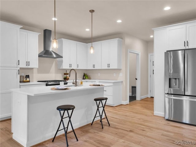 kitchen featuring light hardwood / wood-style flooring, pendant lighting, wall chimney range hood, and appliances with stainless steel finishes