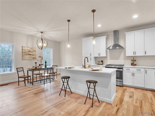 kitchen with pendant lighting, white cabinets, wall chimney range hood, and stainless steel range