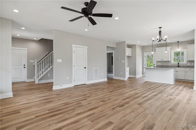 unfurnished living room featuring ceiling fan with notable chandelier, light hardwood / wood-style floors, and sink