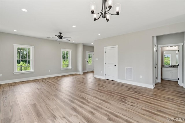 unfurnished living room featuring light hardwood / wood-style flooring, ceiling fan with notable chandelier, and plenty of natural light