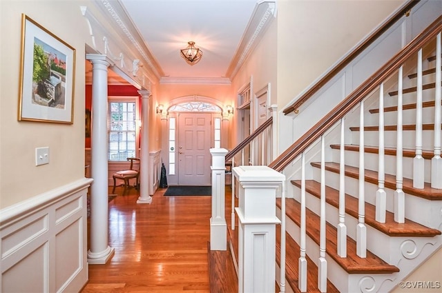 foyer entrance with light wood-type flooring, ornamental molding, stairway, a decorative wall, and decorative columns