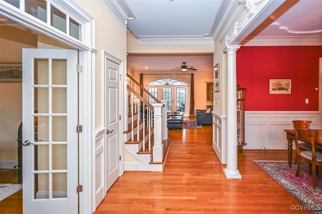 foyer entrance with ornate columns, ornamental molding, ceiling fan, french doors, and light wood-style floors