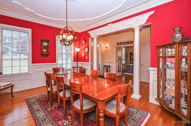 dining room with light wood-style floors, an inviting chandelier, ornamental molding, and ornate columns