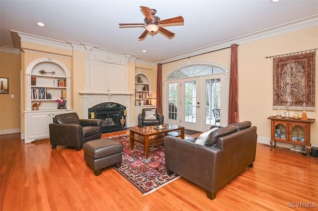 living area featuring light wood finished floors, crown molding, a large fireplace, and ceiling fan