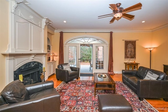 living area with a ceiling fan, wood finished floors, recessed lighting, crown molding, and a premium fireplace