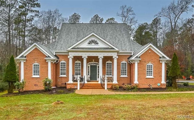 neoclassical / greek revival house with brick siding, covered porch, and a front yard