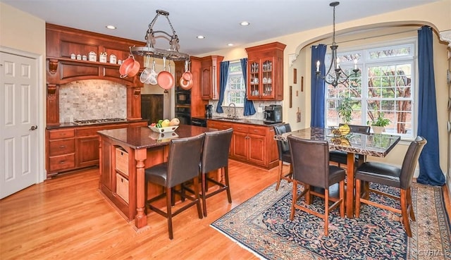 kitchen with a sink, arched walkways, light wood-style flooring, and stainless steel gas cooktop