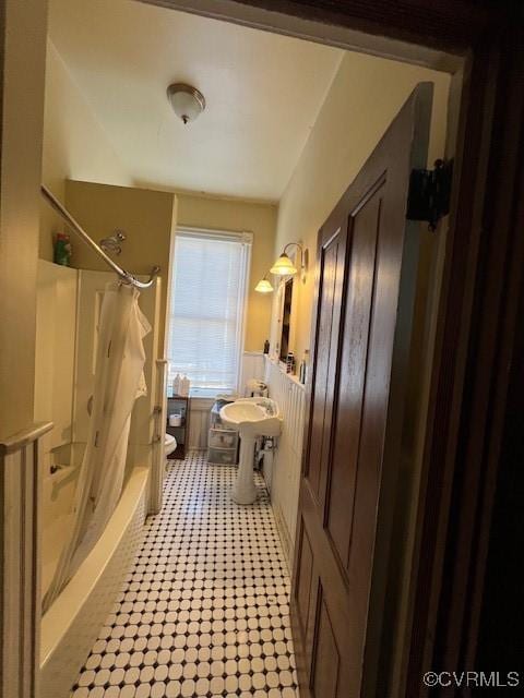 bathroom featuring a wainscoted wall, shower / tub combo with curtain, and toilet