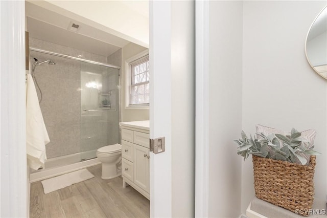 bathroom featuring vanity, wood-type flooring, a shower with shower door, and toilet