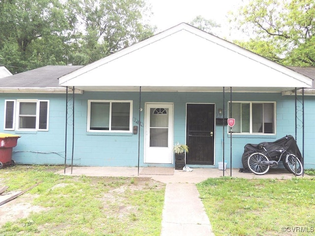 ranch-style home with concrete block siding, covered porch, and a front lawn