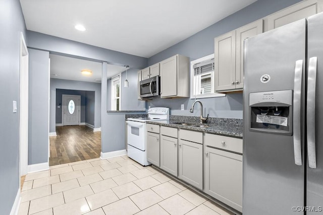 kitchen featuring light wood-type flooring, gray cabinetry, stainless steel appliances, sink, and dark stone countertops