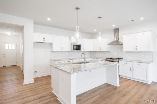 kitchen featuring appliances with stainless steel finishes, decorative light fixtures, white cabinetry, sink, and wall chimney range hood