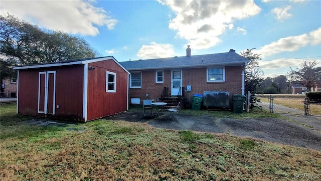 rear view of house with brick siding, entry steps, an outdoor structure, a yard, and a gate