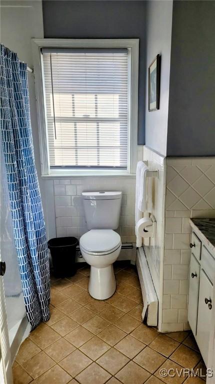 bathroom with tile patterned flooring, toilet, vanity, a stall shower, and tile walls