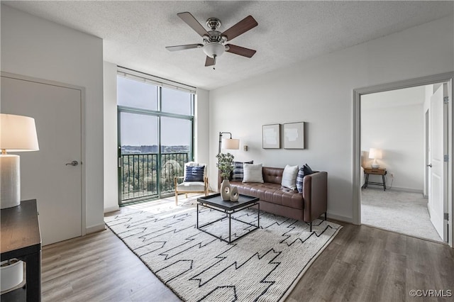 living room with ceiling fan, a wall of windows, wood-type flooring, and a textured ceiling