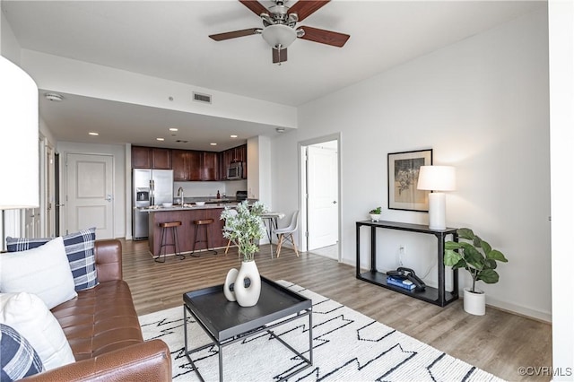 living room featuring light hardwood / wood-style floors, ceiling fan, and sink