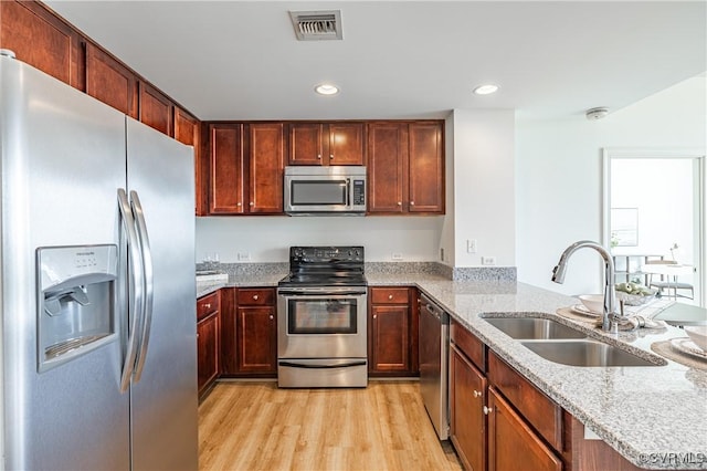 kitchen with light stone countertops, sink, stainless steel appliances, and light wood-type flooring