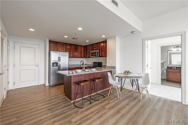 kitchen with light stone counters, kitchen peninsula, a breakfast bar, appliances with stainless steel finishes, and light wood-type flooring