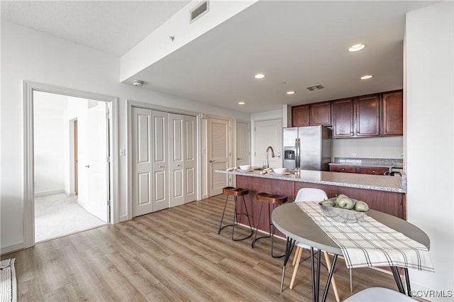 kitchen featuring light stone countertops, stainless steel refrigerator with ice dispenser, a center island with sink, light hardwood / wood-style floors, and a breakfast bar area