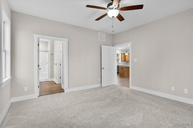 unfurnished bedroom featuring light carpet, connected bathroom, and multiple windows