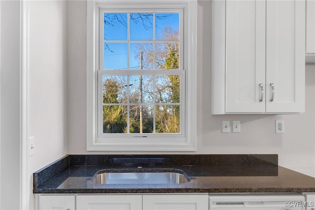 interior details with white cabinets, dark stone counters, dishwasher, and sink