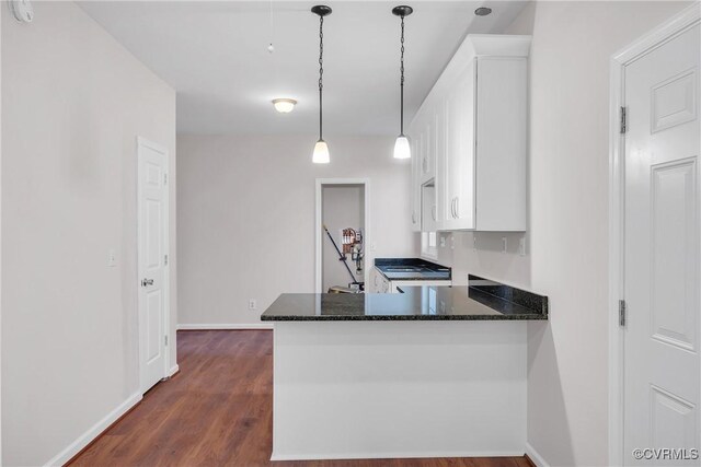 kitchen featuring kitchen peninsula, dark hardwood / wood-style flooring, dark stone counters, pendant lighting, and white cabinets