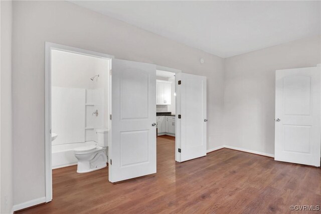 unfurnished bedroom featuring ensuite bathroom and dark hardwood / wood-style floors