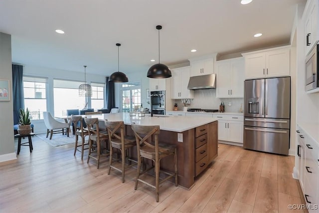 kitchen with a breakfast bar, white cabinetry, hanging light fixtures, stainless steel appliances, and a center island with sink