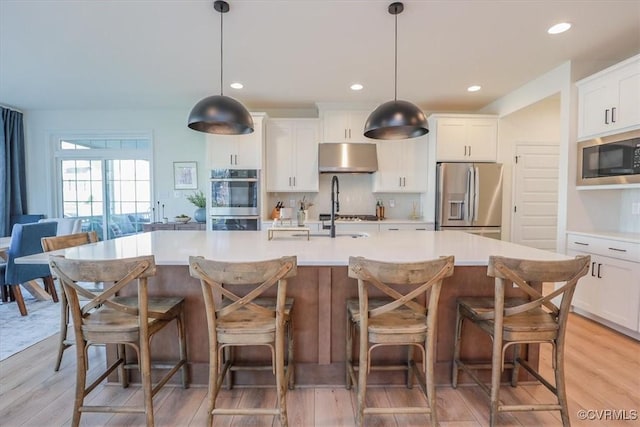 kitchen featuring stainless steel appliances, hanging light fixtures, and light hardwood / wood-style flooring