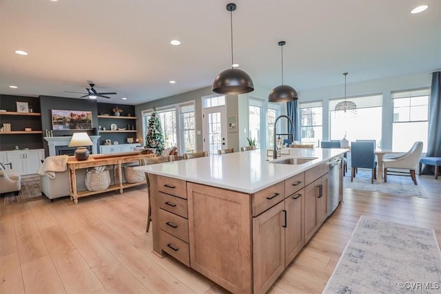 kitchen with light brown cabinetry, decorative light fixtures, sink, a kitchen island with sink, and built in shelves