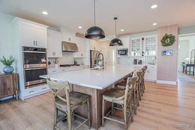 kitchen with appliances with stainless steel finishes, decorative light fixtures, white cabinetry, an island with sink, and a kitchen bar