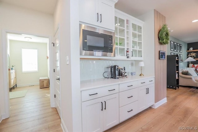 bar with built in microwave, white cabinetry, tasteful backsplash, and light hardwood / wood-style flooring