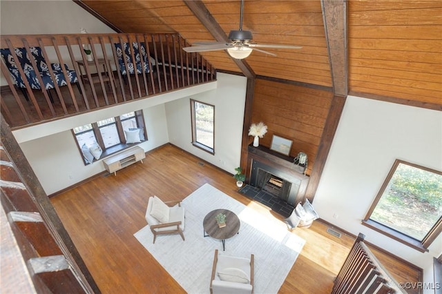 living room featuring beam ceiling, ceiling fan, wooden ceiling, hardwood / wood-style floors, and a fireplace